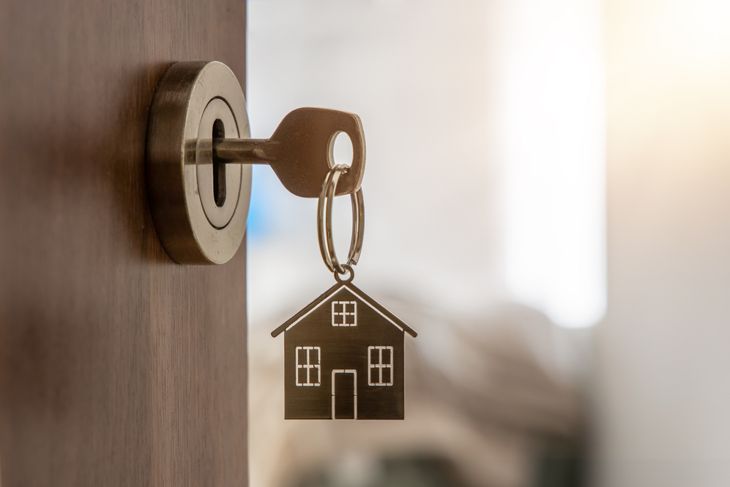 Concept of a secured loan. Open door to a new home with key and home shaped keychain
