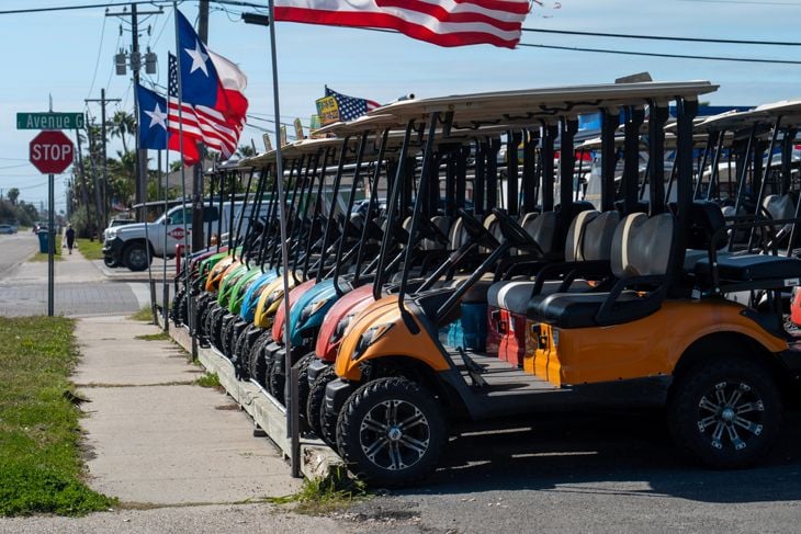 Colorful rental golf carts, lined up along the sidewalk and ready for rent