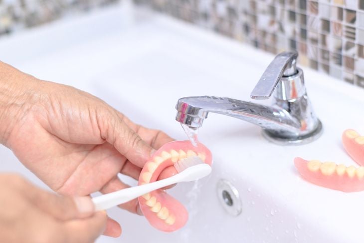 Brush old woman hand to clean denture