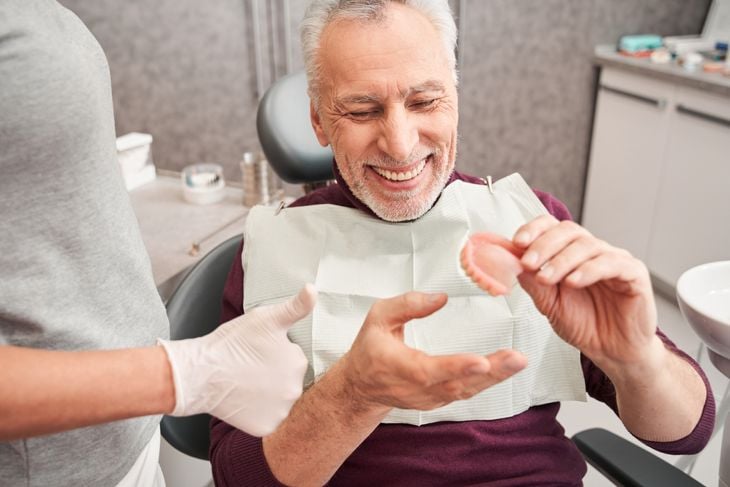 Cropped view of the dentist showing to senior grey haired patient teeth dentures while working at the dental clinic