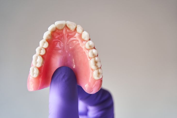 Fingers in purple gloves holding set of dentures