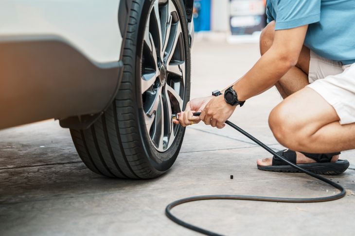 A person kneeling and inflating tires of vehicle