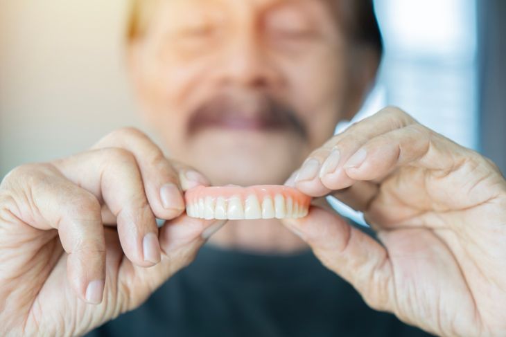 Grey haired senior man holding orthodontic prosthesis denture with a happy face standing and smiling with a confident