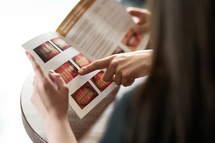 dentist and patient are looking at magazine with photographs of teeth