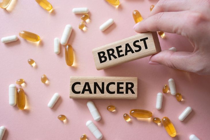 A hand arranges wooden blocks labeled “breast” and “cancer” on a table scattered with capsules and softgel pills—illustrating breast cancer treatment choices and the variety of approaches available. 