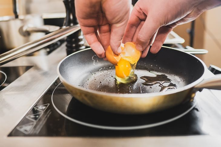 A close-up of hands cracking an egg into a frying pan on a modern stove.