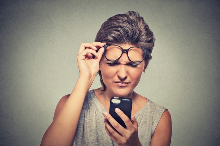 Closeup portrait headshot young woman with glasses having trouble seeing cell phone has vision problems