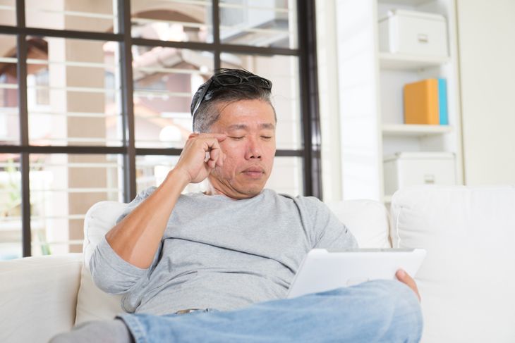 asian man with eyes problem after long hours of using computer tablet