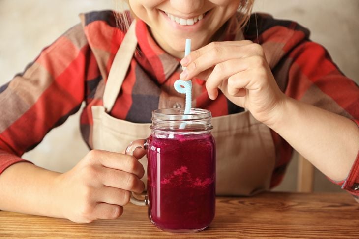 Young woman drinking beet smoothie while sitting at table