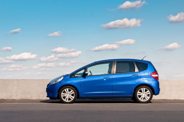 Blue car Honda Jazz parked on the road against the background of the sunny sky
