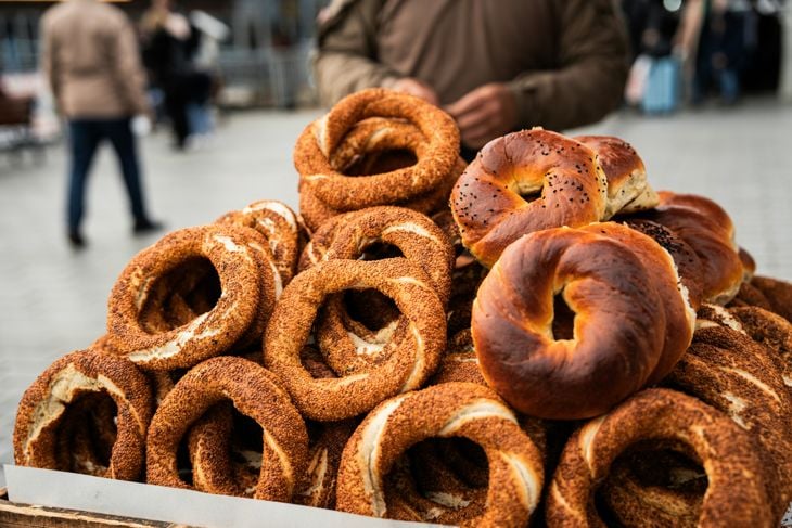 Stack of golden-brown simit, a circular Turkish bread covered with sesame seeds, on a street vendor's tray.