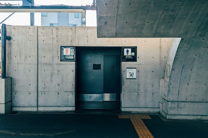 Concrete entrance to a public restroom with separate signs for male, female, and wheelchair accessible stalls.