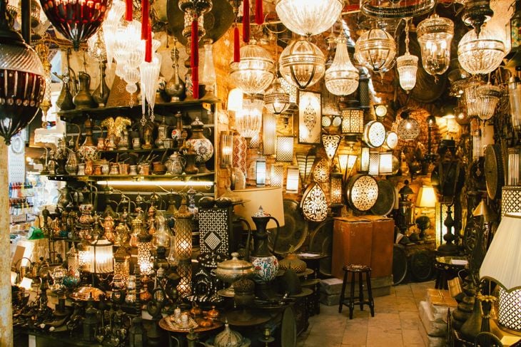 A market stall filled with various hanging lanterns and decorative metal crafts illuminated warmly.