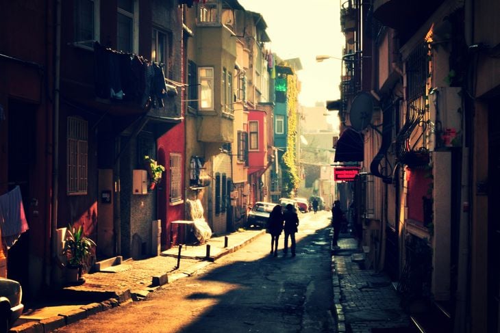 Narrow sunlit street with colorful buildings and two people walking in the distance during golden hour.