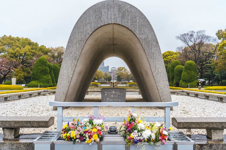 The Cenotaph for the A-bomb victims at Hiroshima Peace Memorial Park with flowers placed in front.