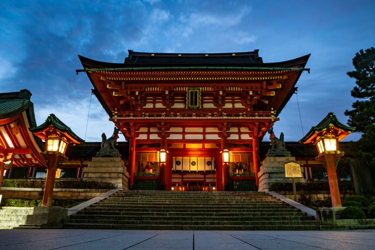 Traditional Japanese shrine illuminated at dusk with symmetrical stone steps and lanterns on both sides.