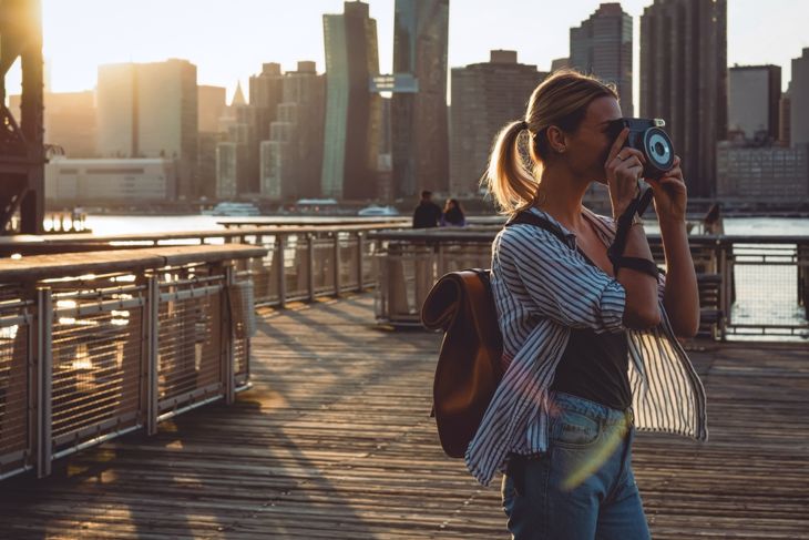 Young female tourist with rucksack taking pictures of evening city