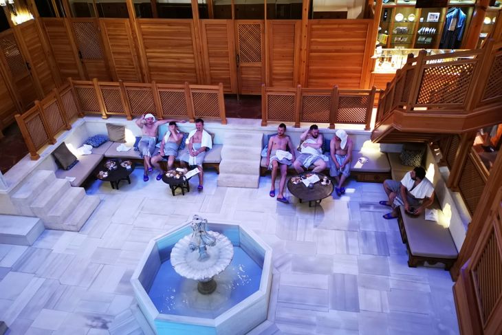 Luxury room with wooden walls, marble floor, octagonal fountain, sofas, and guests seated nearby.