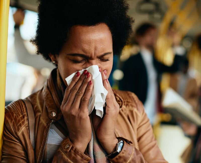 Ill black woman using tissue and blowing nose while commuting by bus.