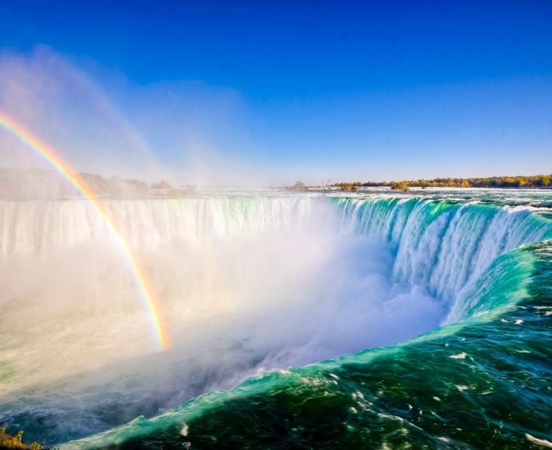 A rainbow shows in the bright daytime mist that hangs around Niagara Falls, viewed from Ontario, Canada.