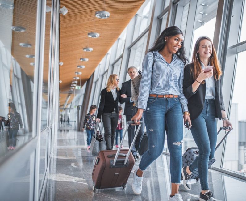Two female friends talking as they walk through an airport with luggage