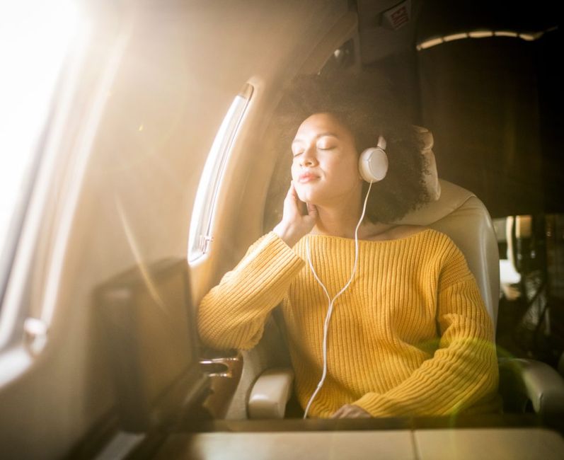 Woman in headphones closing her eyes on an airplane