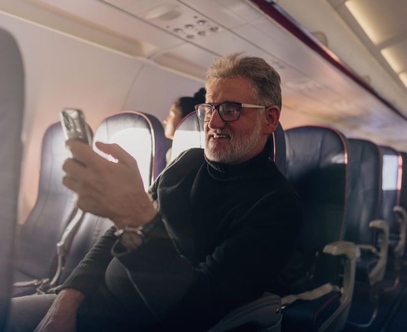 Senior man with beard sitting in airplane aisle seat using a phone