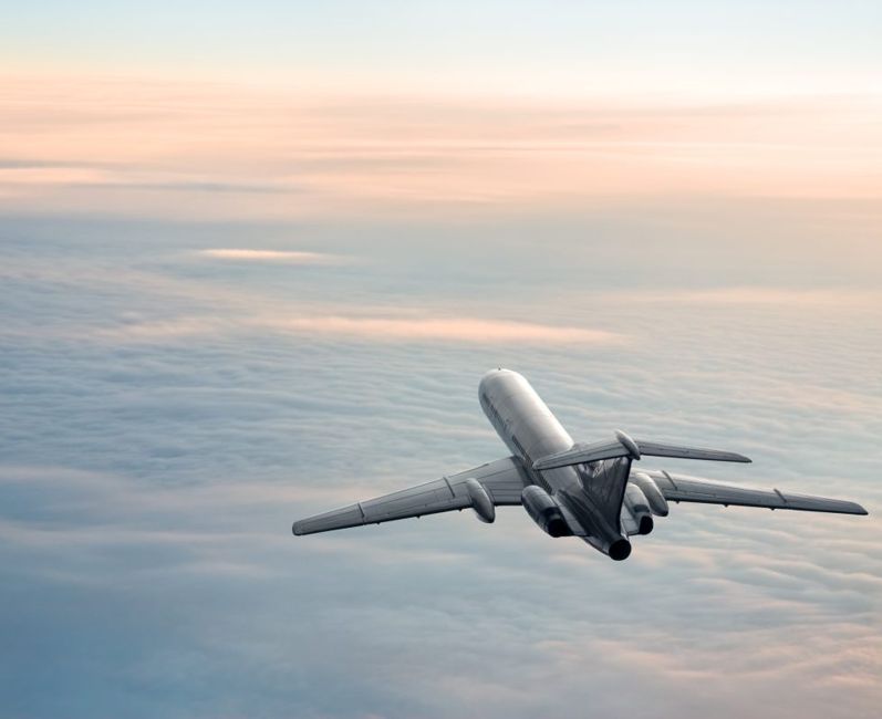 An airplane flies high above the clouds with the rising sun on the horizon