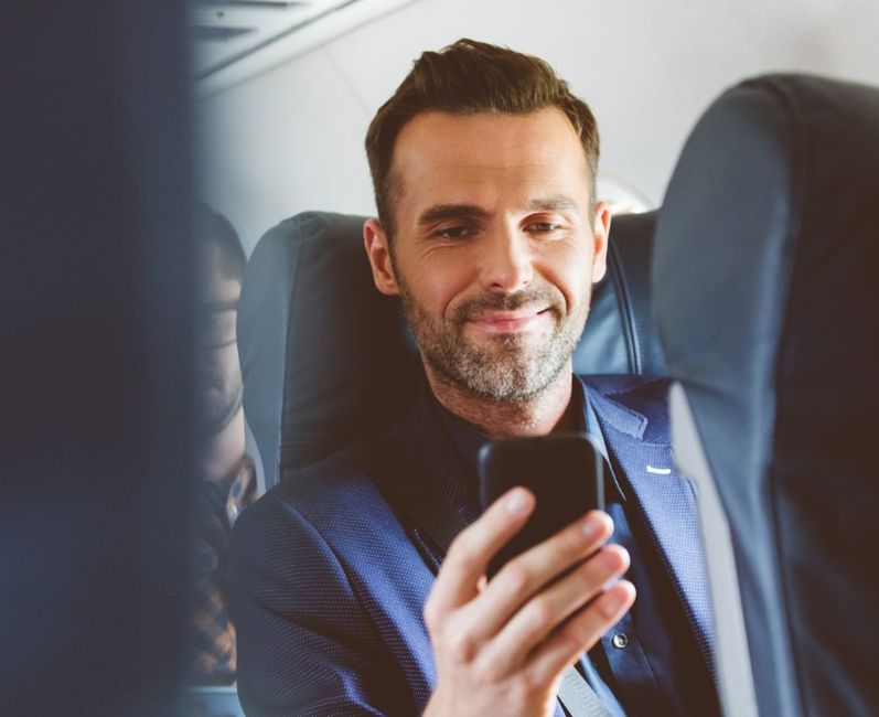 Man sitting in an airplane seat and looking at a smartphone
