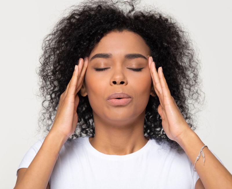 Nervous african woman breathing calming down relieving headache or managing stress, black girl feeling stressed self-soothing massaging temples exhaling isolated on white grey studio blank
