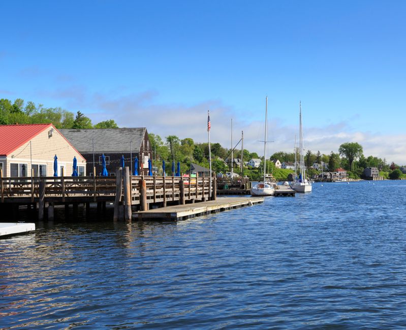 Cafe Deck with Umbrellas on Penobscot Bay Harbor with boats and dock in summer, Castine, Maine, New England, USA, June 14, 2019