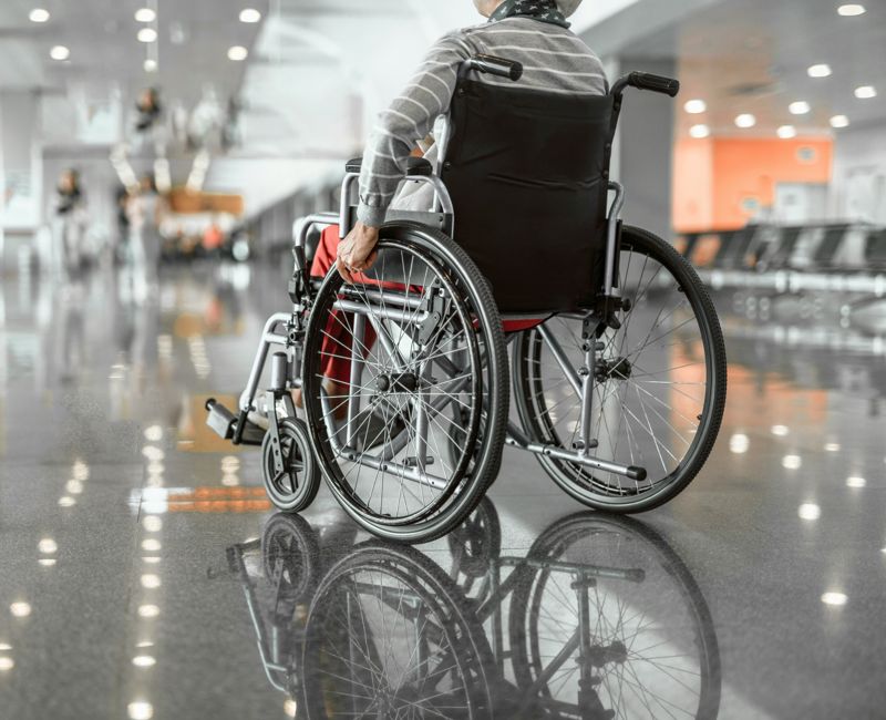 Back view photo of old woman moving in wheelchair in the lobby at airport. Copy space in left side