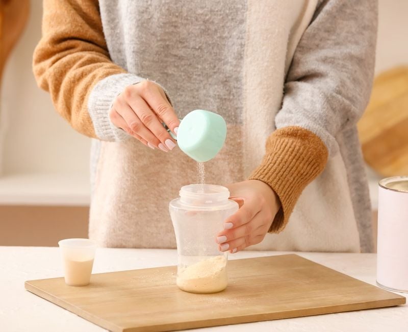 Woman preparing baby milk formula in kitchen 
