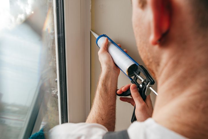 man in overalls sealing cracks to prevent cockroaches